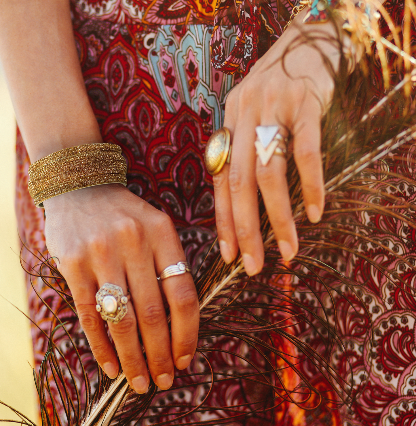 Close-up of hands with multiple rings and bracelets on a patterned fabric background