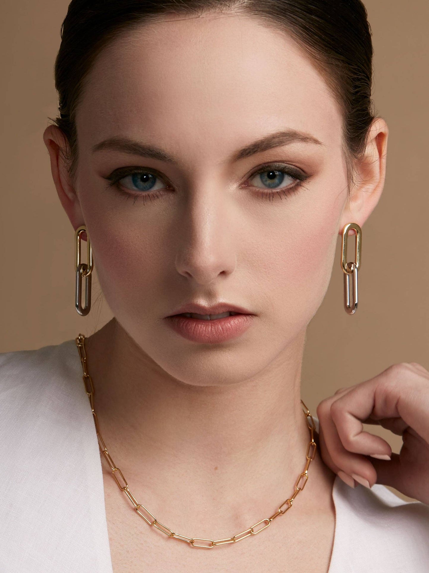 Woman wearing gold chain necklace and earrings against a beige background