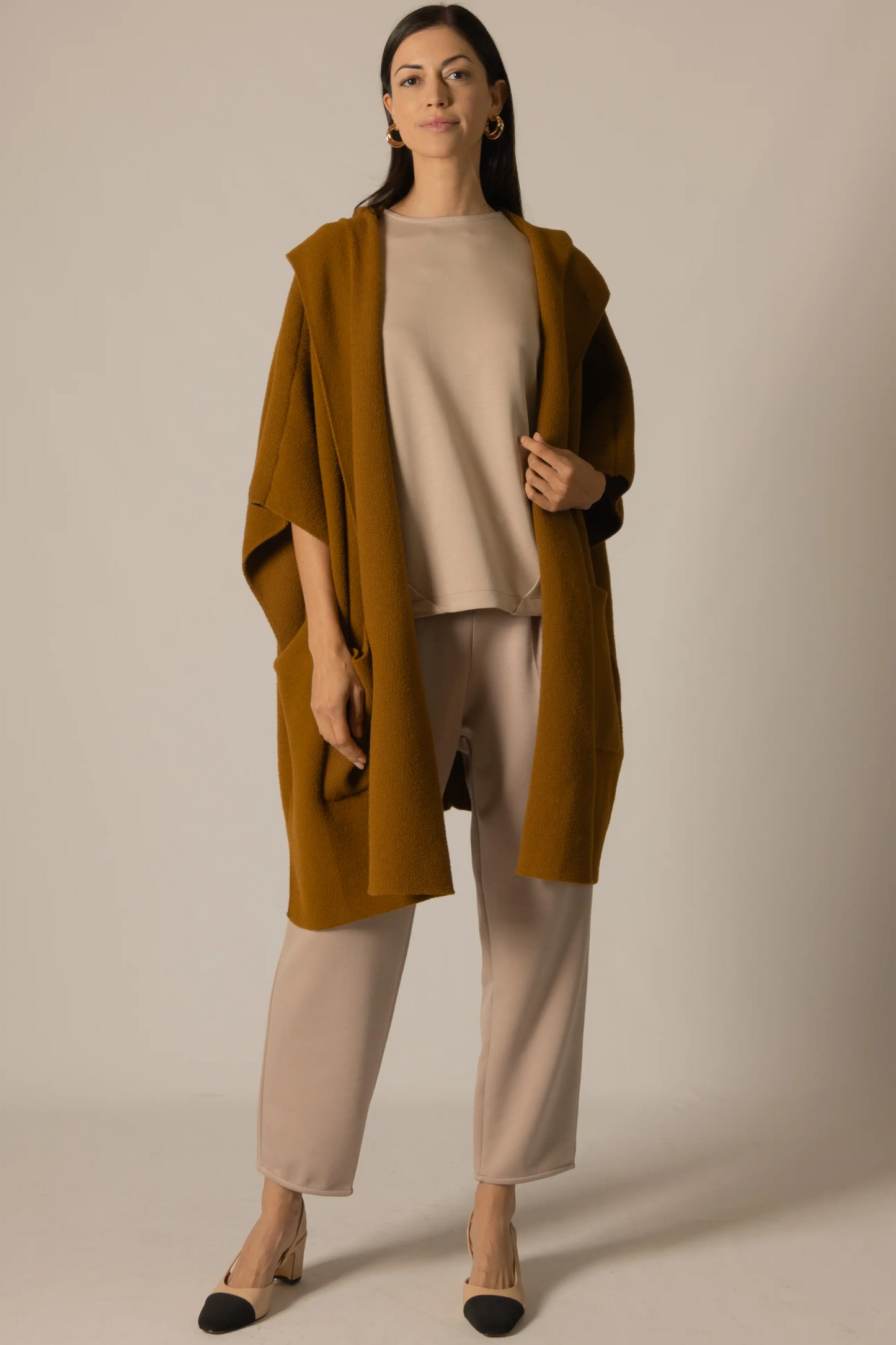 Woman wearing a mustard yellow cardigan over a beige outfit on a plain background