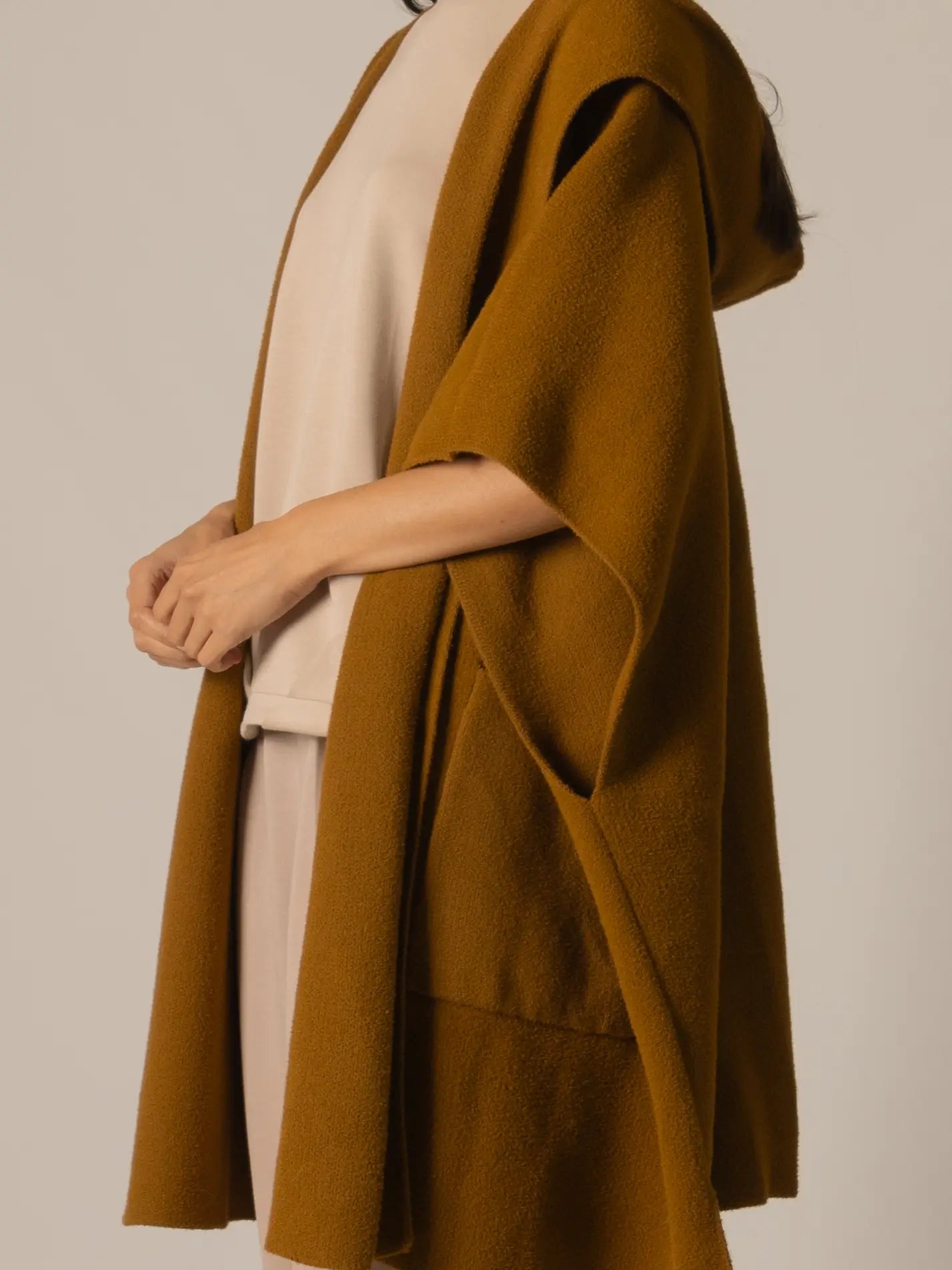 Person wearing a mustard yellow coat over a beige outfit on a plain background