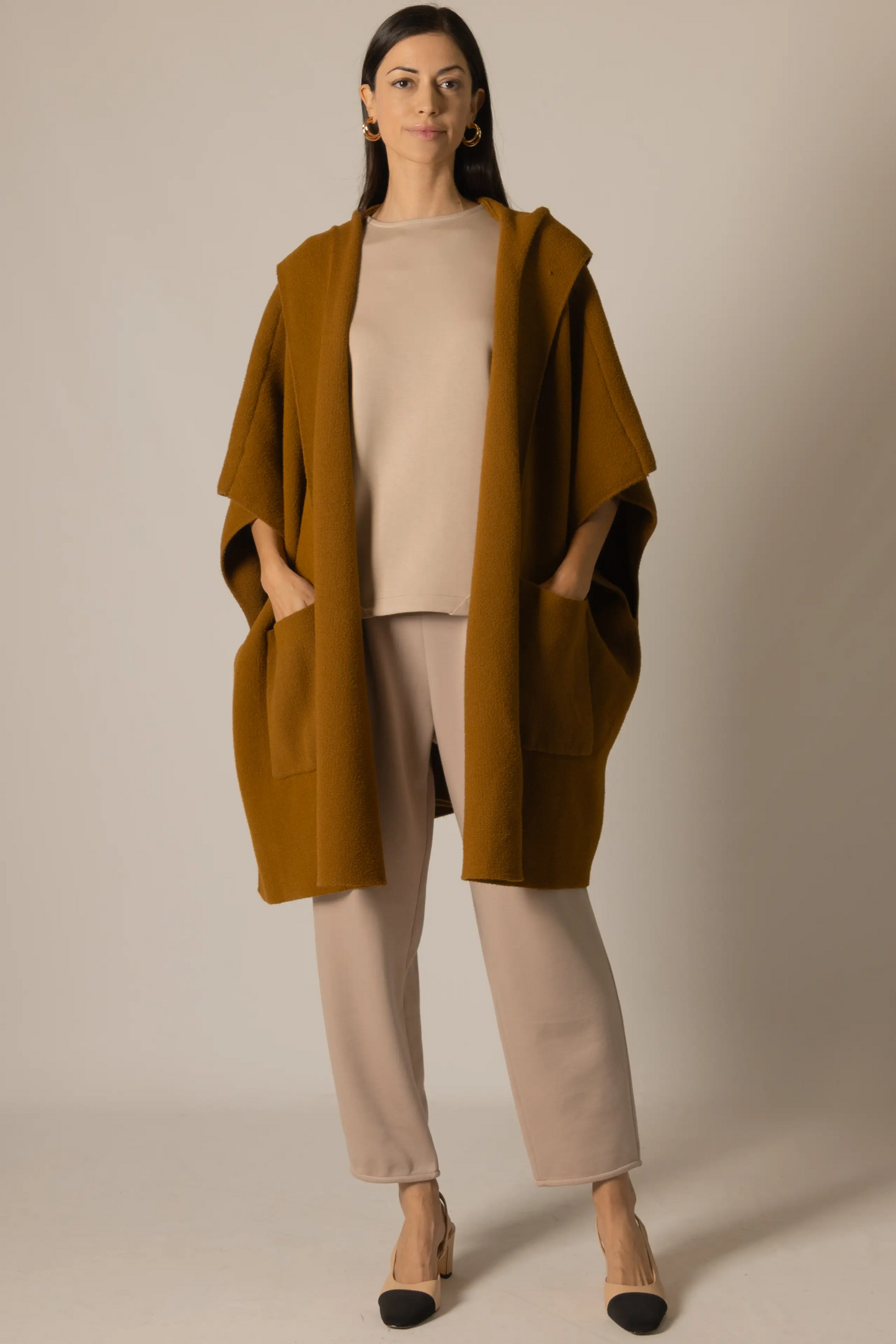 Woman wearing a mustard yellow hooded coat over a beige outfit on a plain background