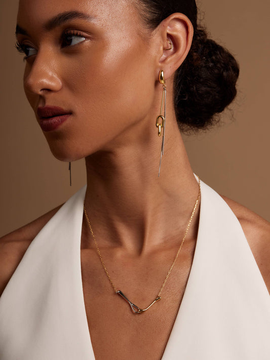 Woman wearing gold earrings and necklace against a neutral background