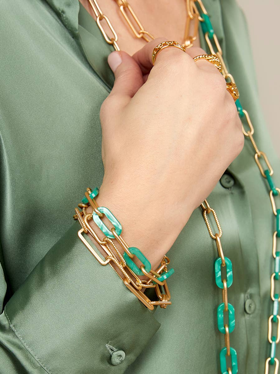 Hand wearing gold and turquoise chain bracelets on a green shirt background