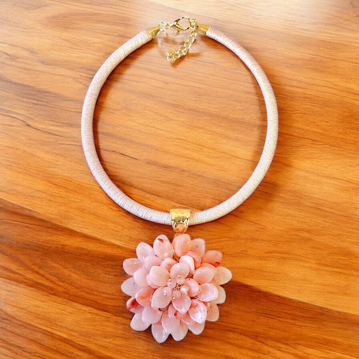 Necklace with a pink floral pendant on a wooden surface