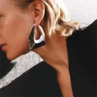 Close-up of polished U-shaped ear studs in shiny copper alloy with a bold design.