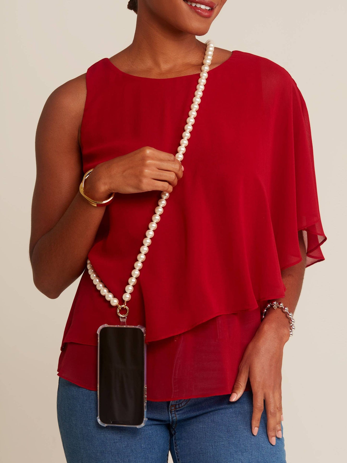Person wearing a red top with a pearl necklace and holding a phone case.