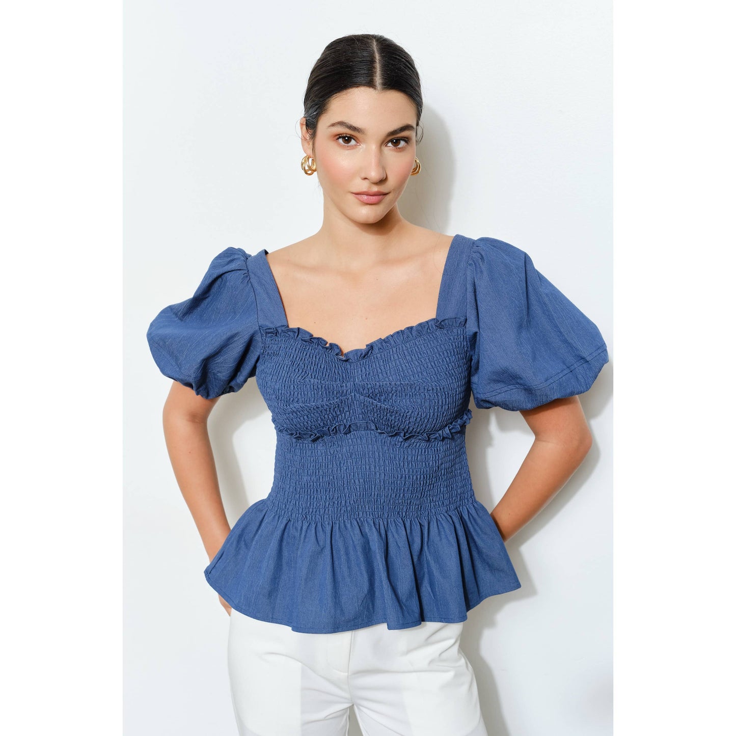 Woman wearing a blue smocked top with puffed sleeves on a white background