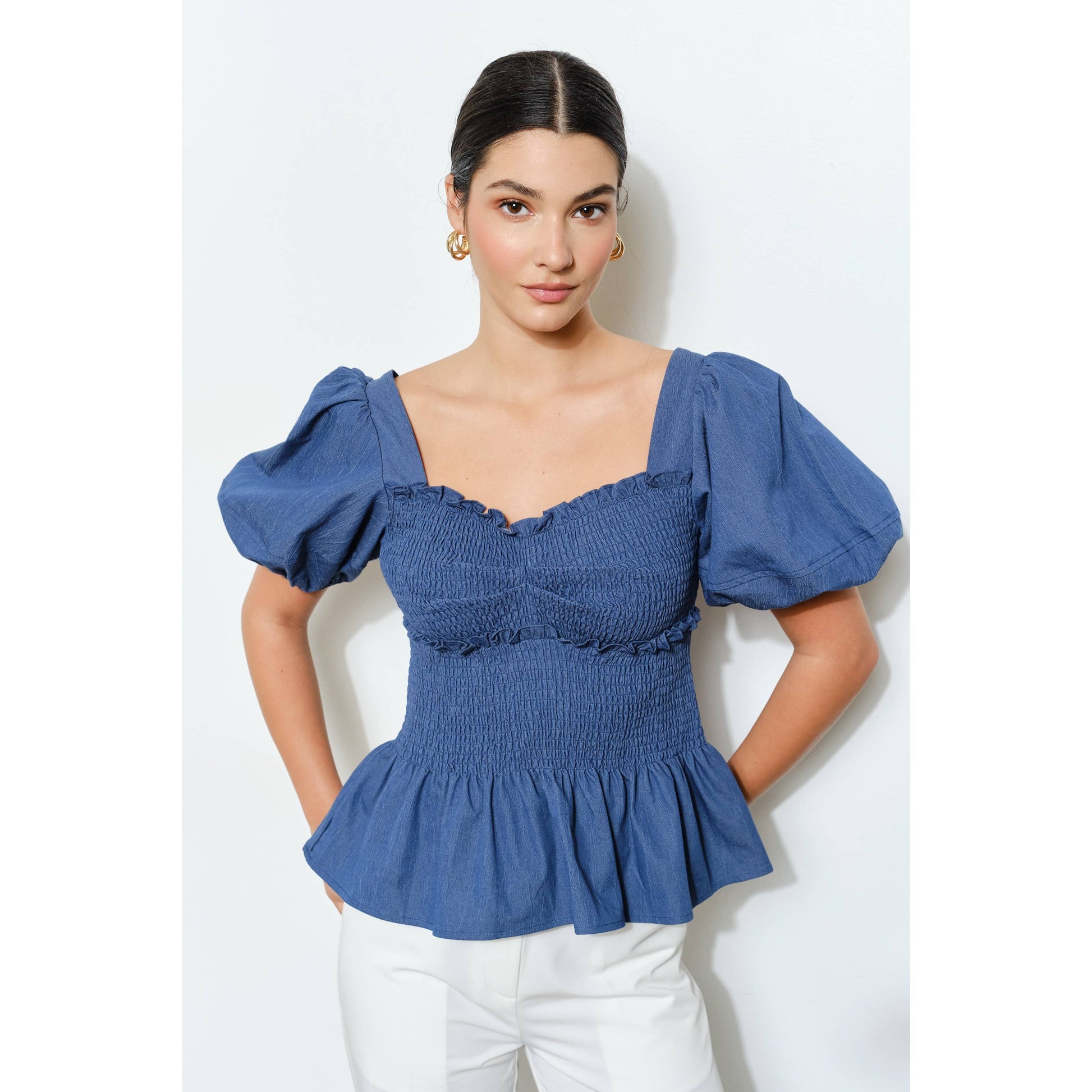 Woman wearing a blue smocked top with puffed sleeves on a white background
