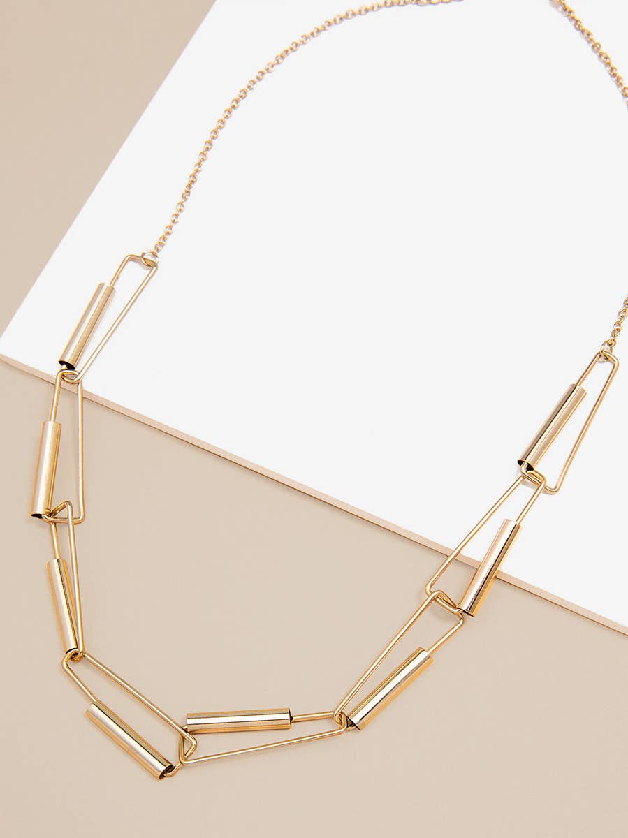 Gold chain necklace on a beige surface with a white paper background