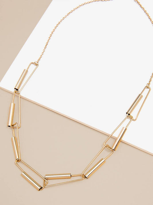 Gold chain necklace on a beige surface with a white paper background