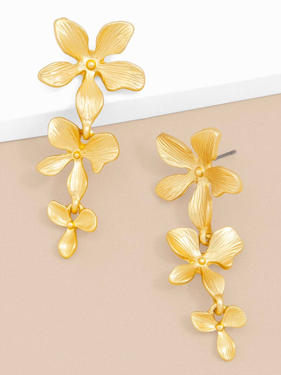 Gold floral earrings on a beige background
