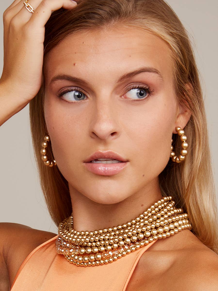 Woman wearing gold jewelry including earrings and a necklace against a neutral background