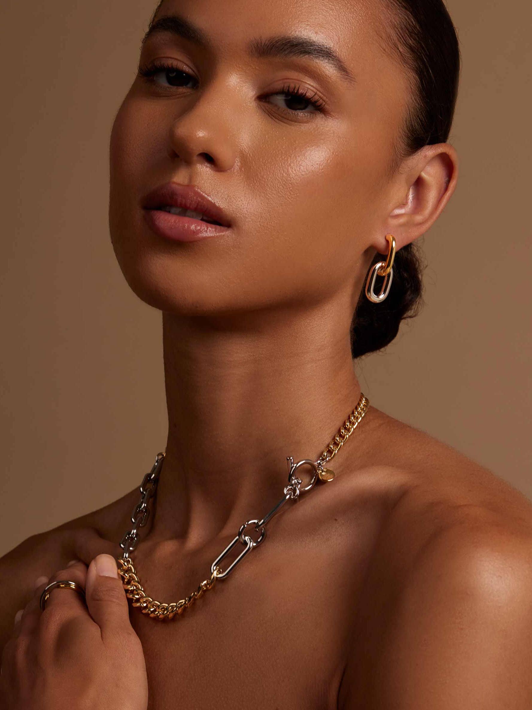 Woman wearing gold necklaces and earrings against a neutral background