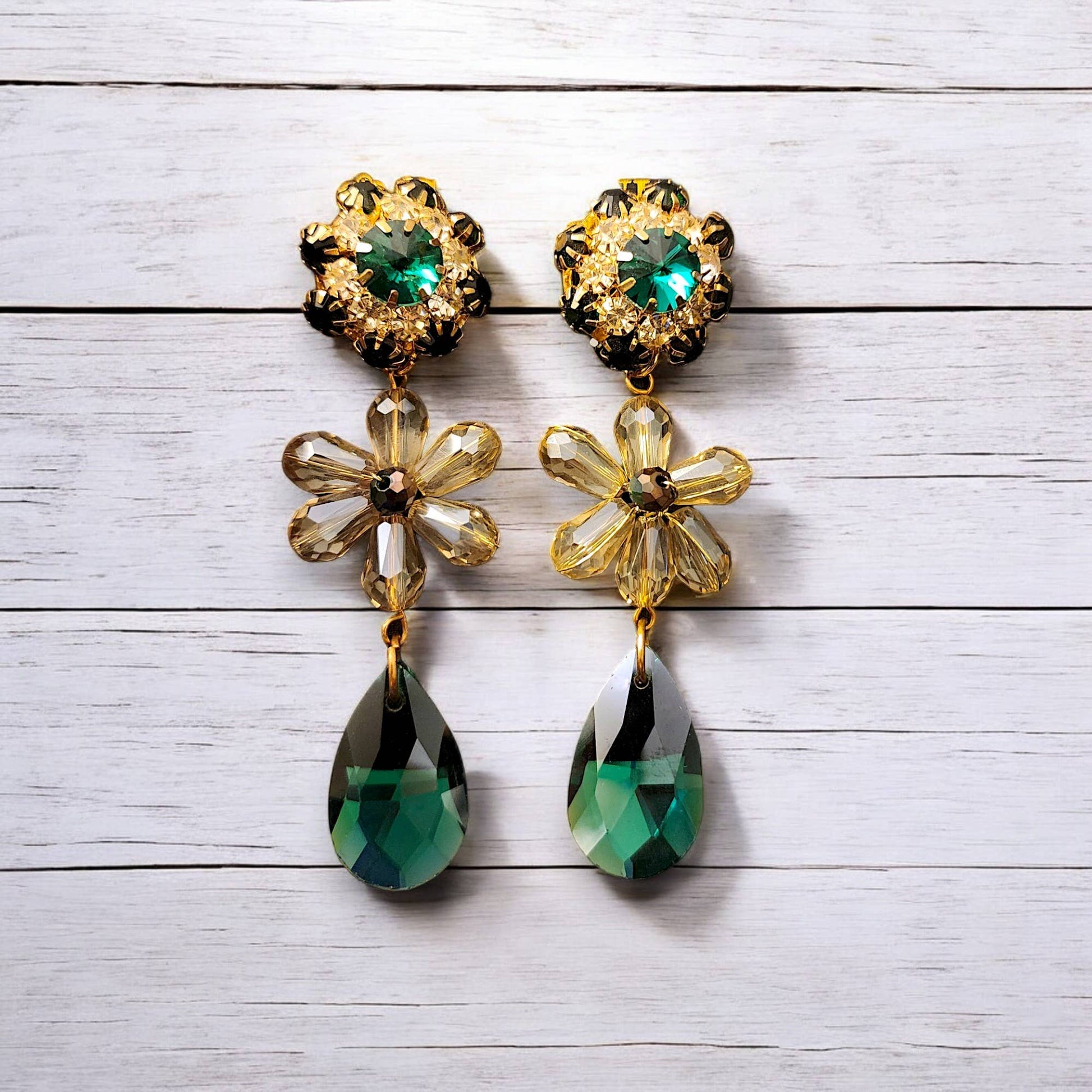 Pair of floral earrings with green teardrop drops on a light wooden surface