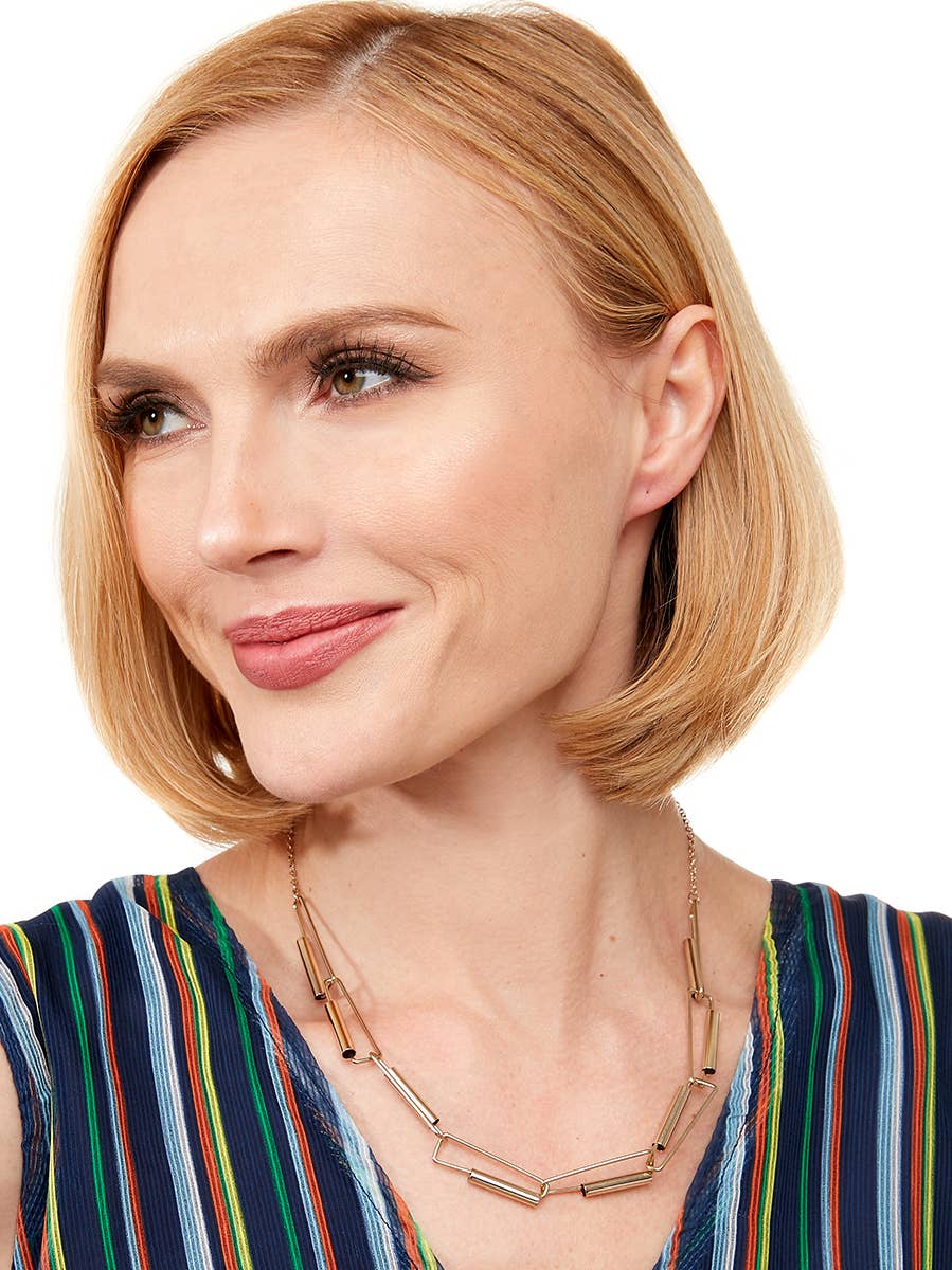 Woman with a short blonde bob wearing a colorful striped top and gold necklace on a white background