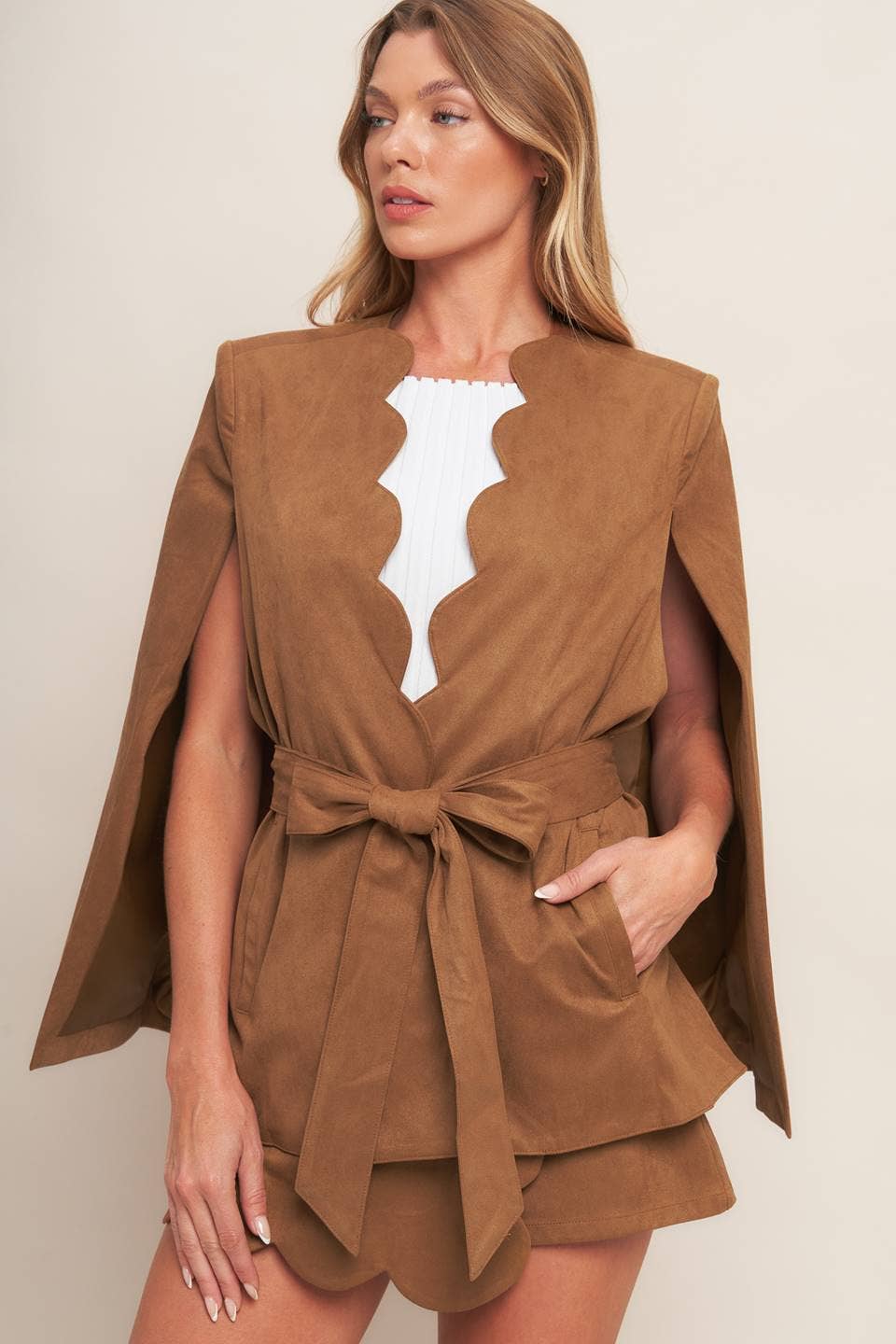 Woman wearing a brown cape outfit against a beige background