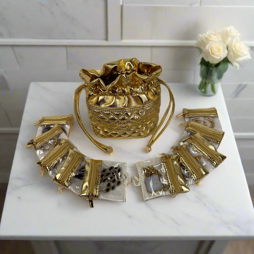 Gold handbag and accessories on a marble surface with a white cabinet and flowers in the background
