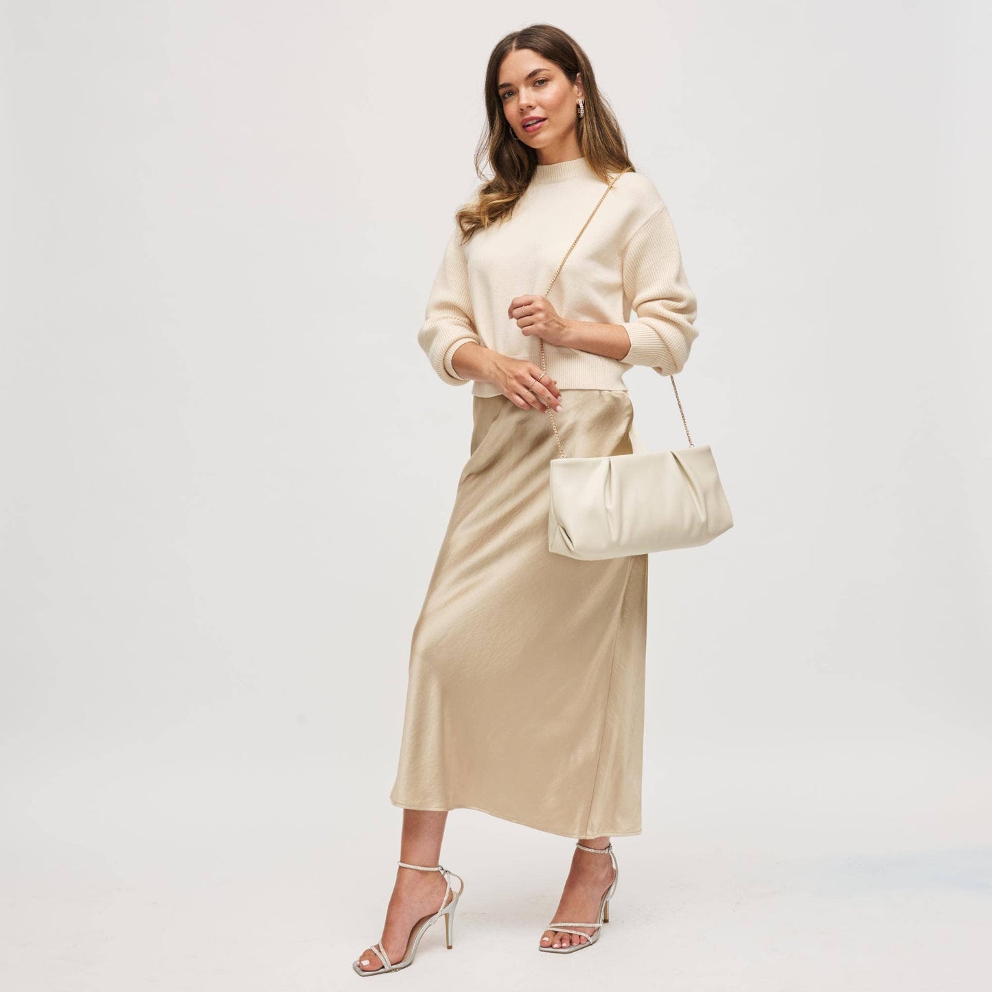 Woman wearing a beige sweater and satin skirt with a matching handbag on a white background