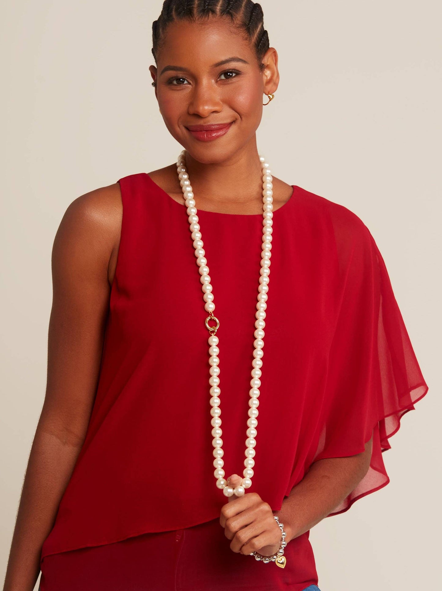Woman wearing a red top and holding a long pearl necklace against a beige background