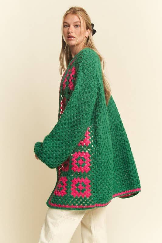 Woman wearing a green crochet cardigan with pink floral patterns on a beige background
