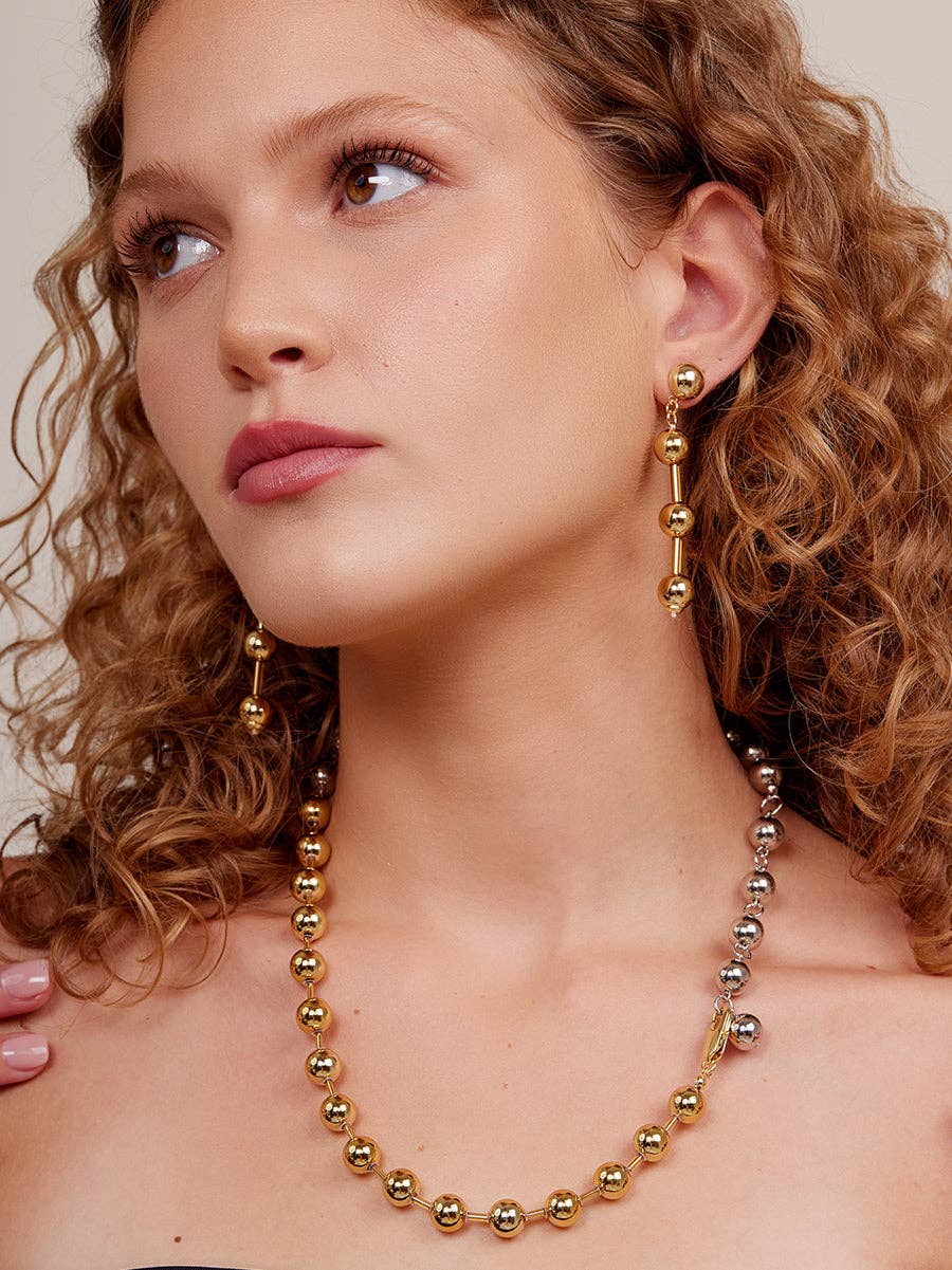 Woman wearing a gold beaded necklace and earrings against a neutral background