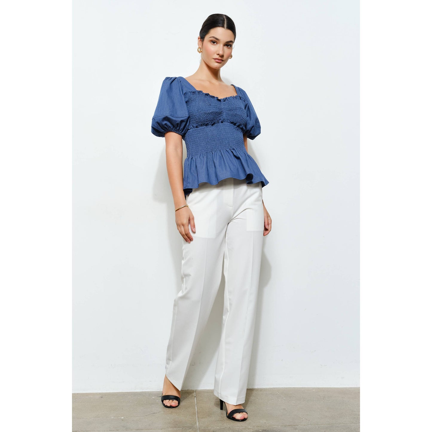 Woman wearing a blue top and white pants against a white background