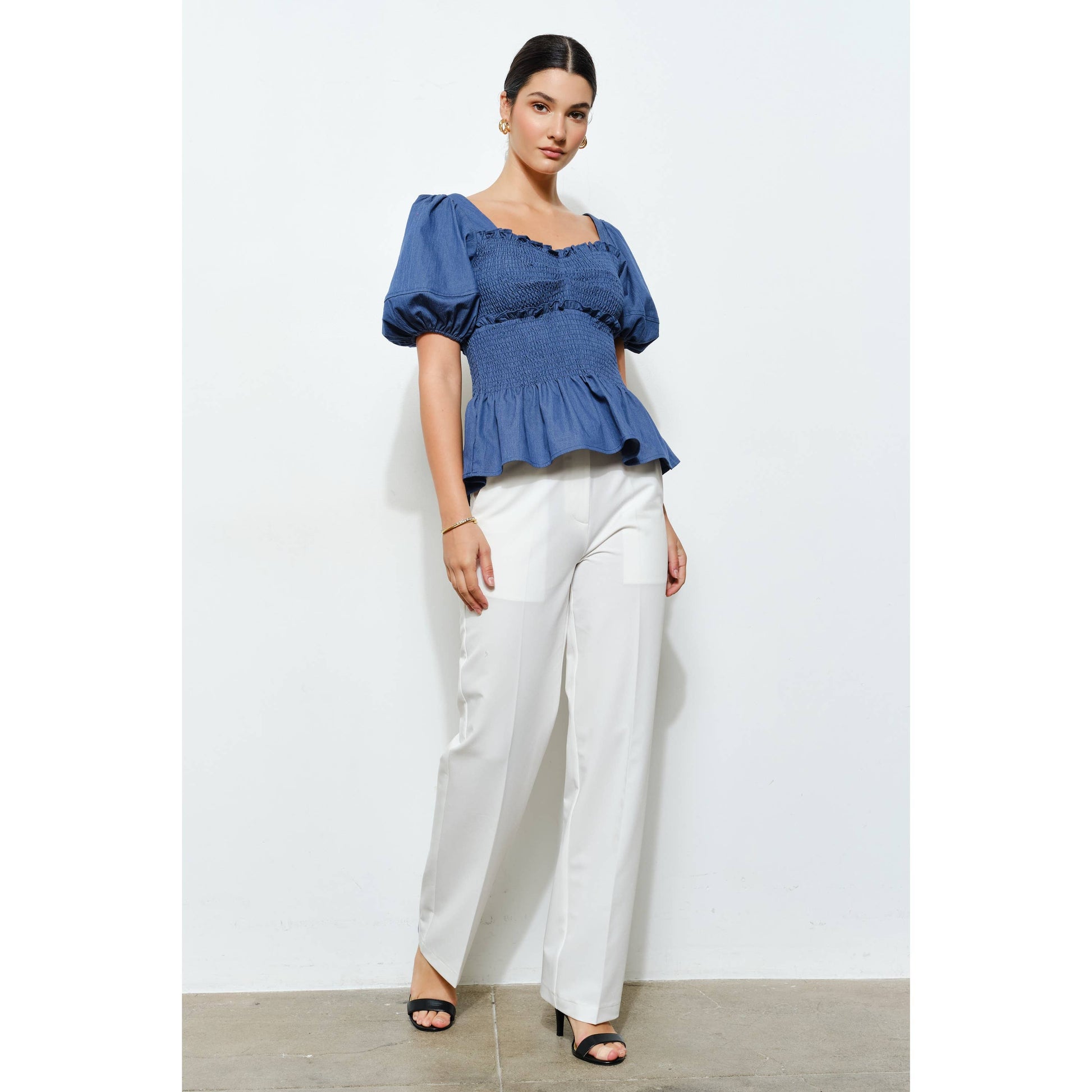 Woman wearing a blue top and white pants against a white background