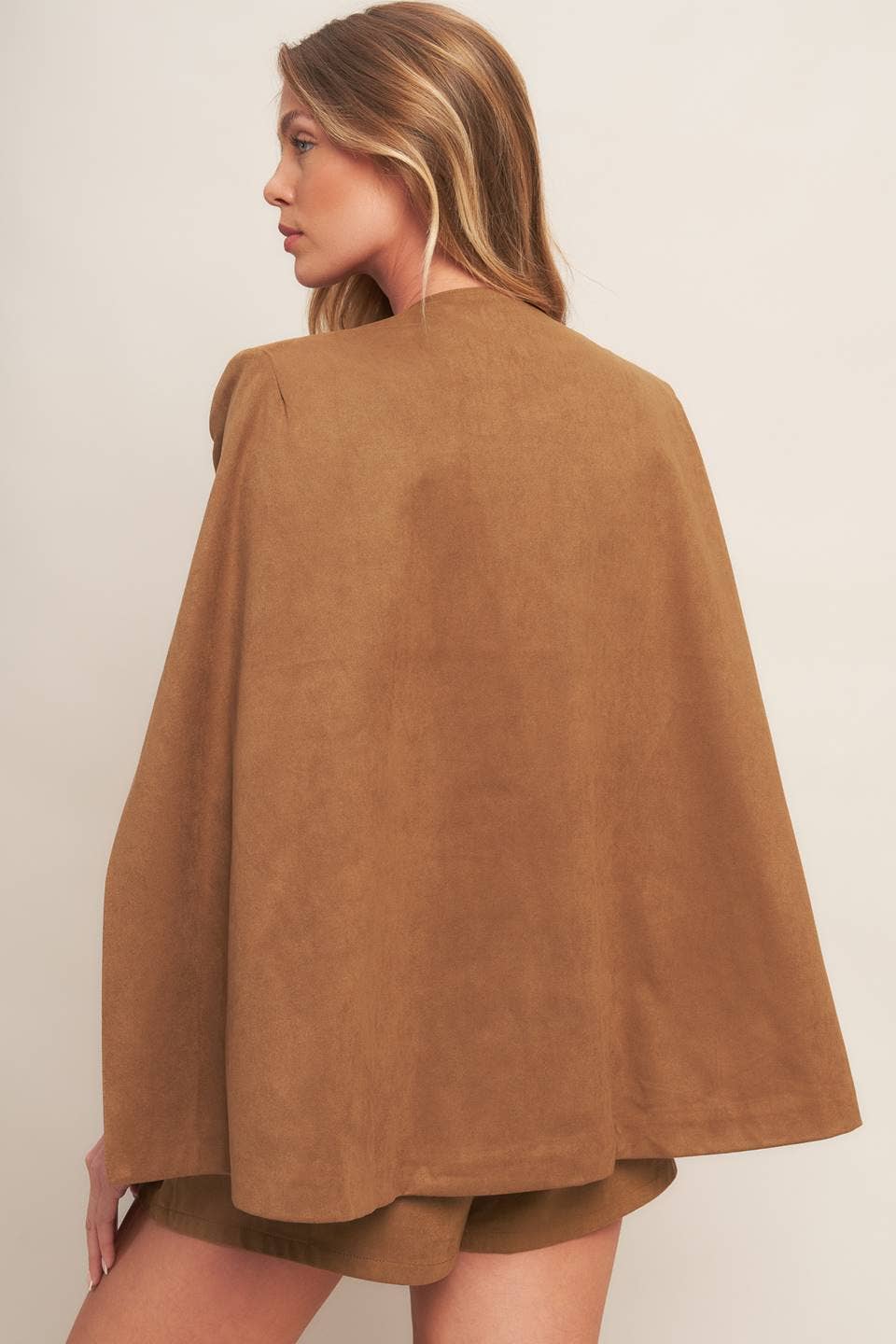 Woman wearing a brown suede cape against a plain background