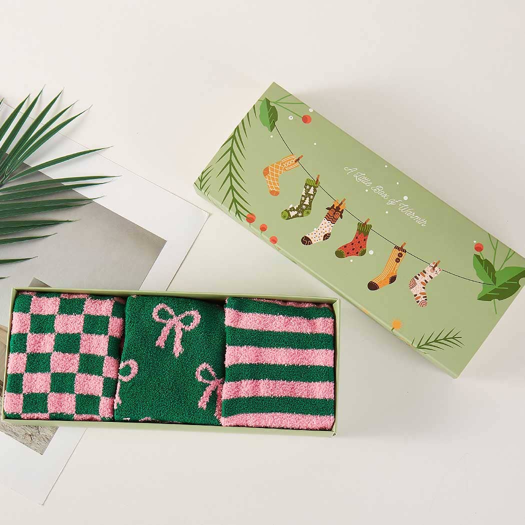 Two pairs of green and pink socks in a decorative box with a festive design on a white background.