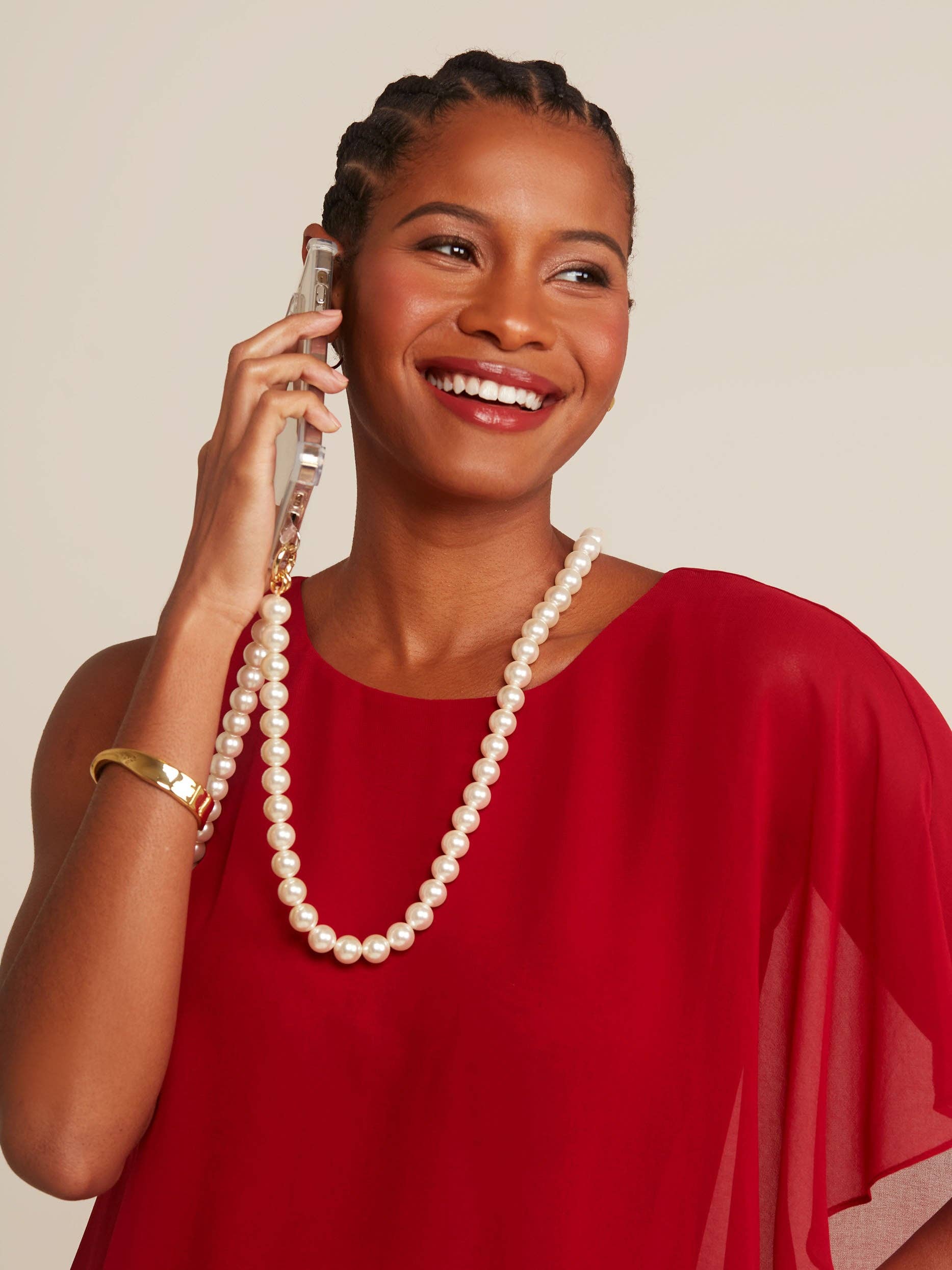 Woman in a red dress with a pearl necklace talking on a vintage phone against a beige background