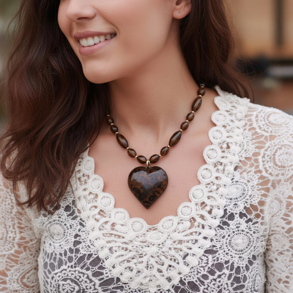 Woman wearing a necklace with a heart-shaped pendant, smiling outdoors.