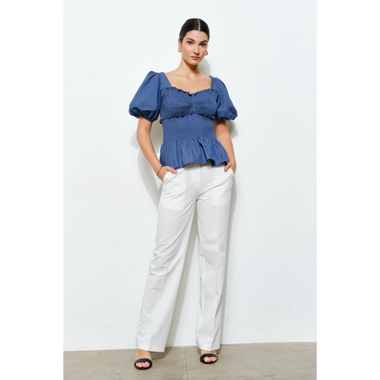 Woman wearing a blue top and white pants against a white background