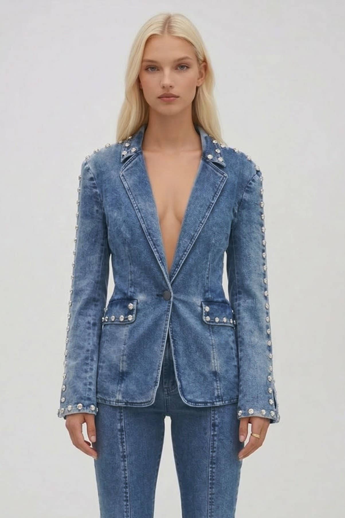 Woman wearing a blue denim blazer with embellishments on a plain background