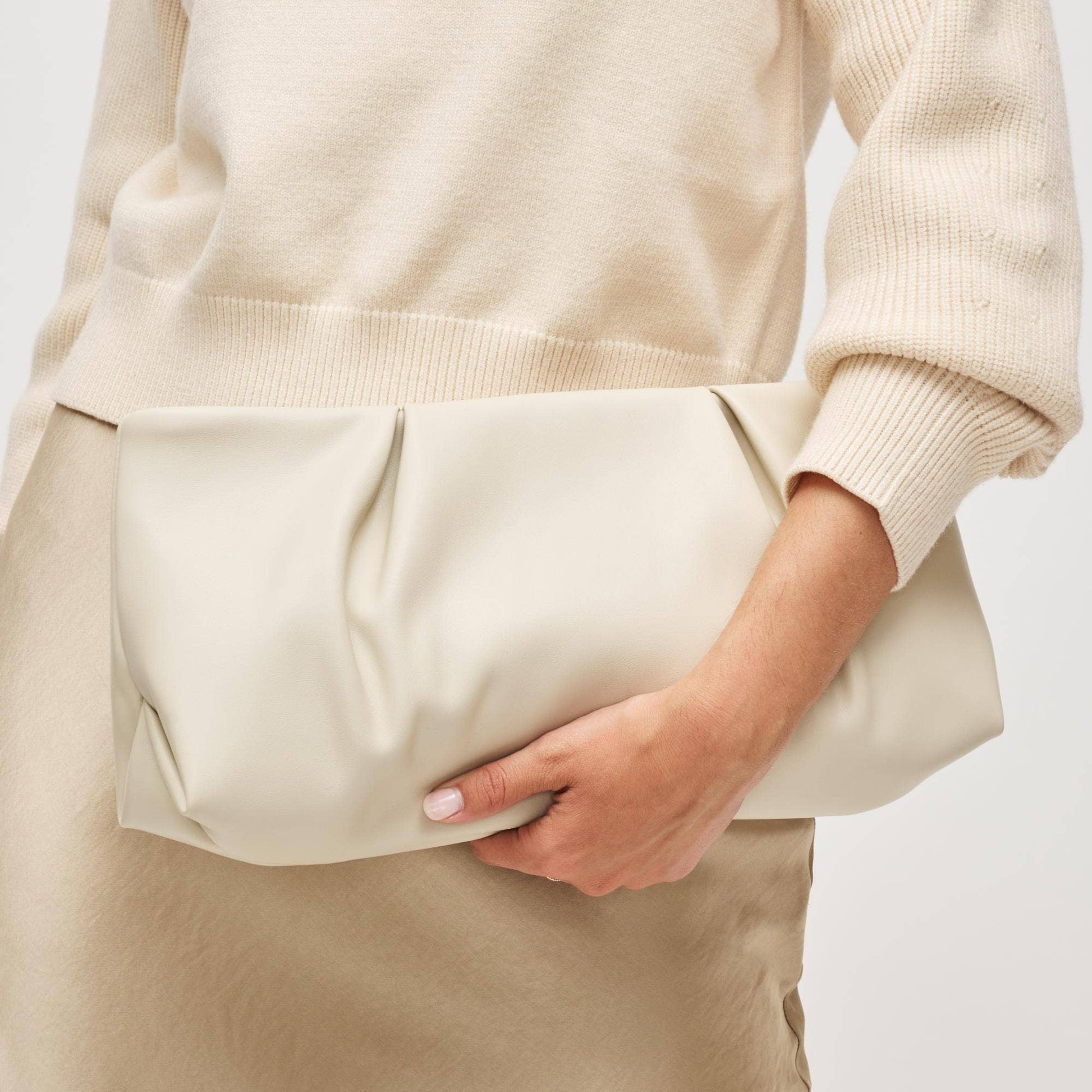 Person wearing a beige sweater and pants with a neutral background