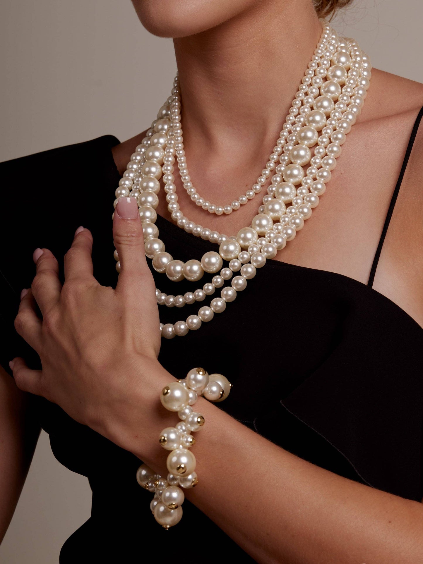 Person wearing multiple pearl necklaces and a bracelet against a neutral background