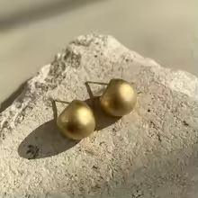 Pair of matte gold dome stud earrings displayed on a textured stone.