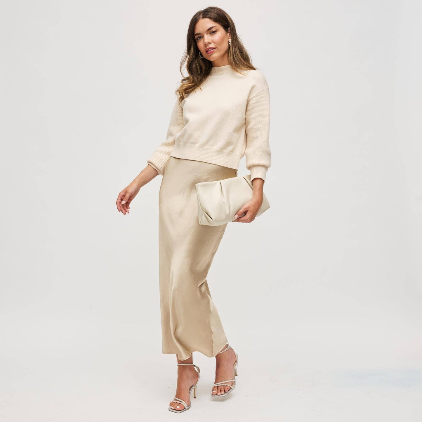 Woman wearing a beige outfit with a matching clutch against a white background