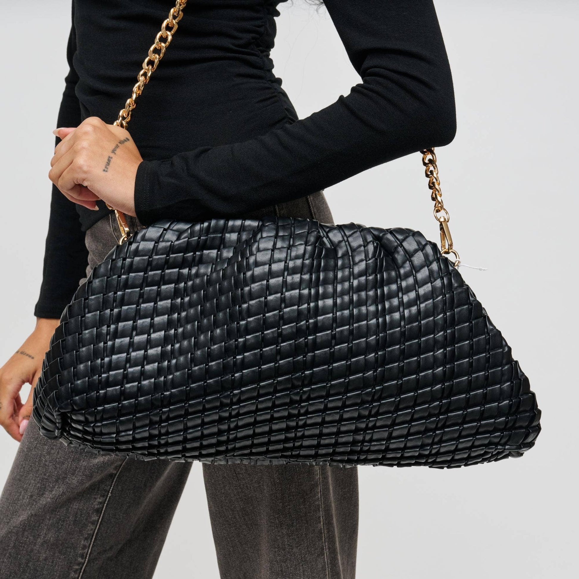 Person holding a black woven handbag with a gold chain strap on a white background