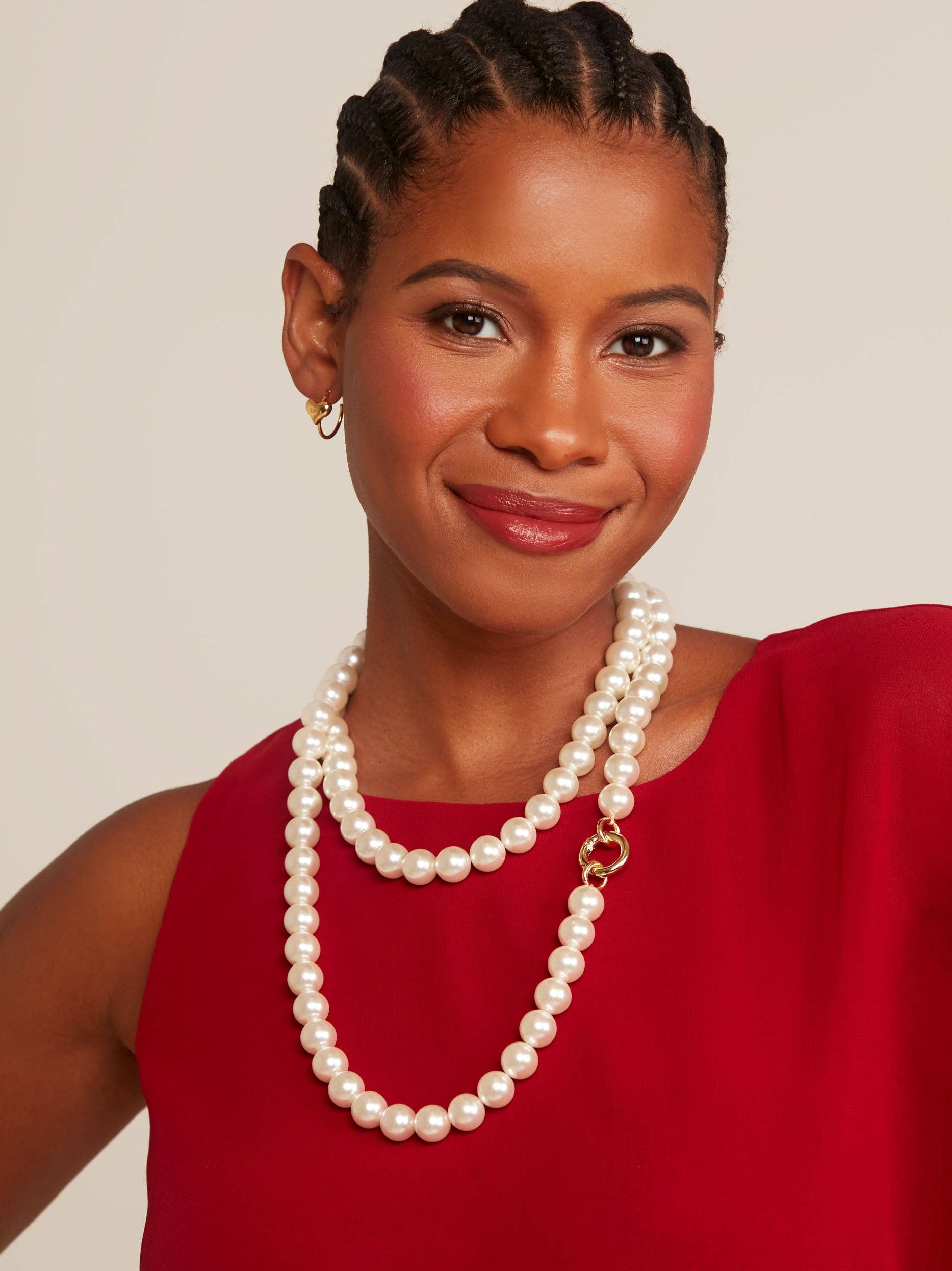 Woman wearing a pearl necklace and red top against a beige background