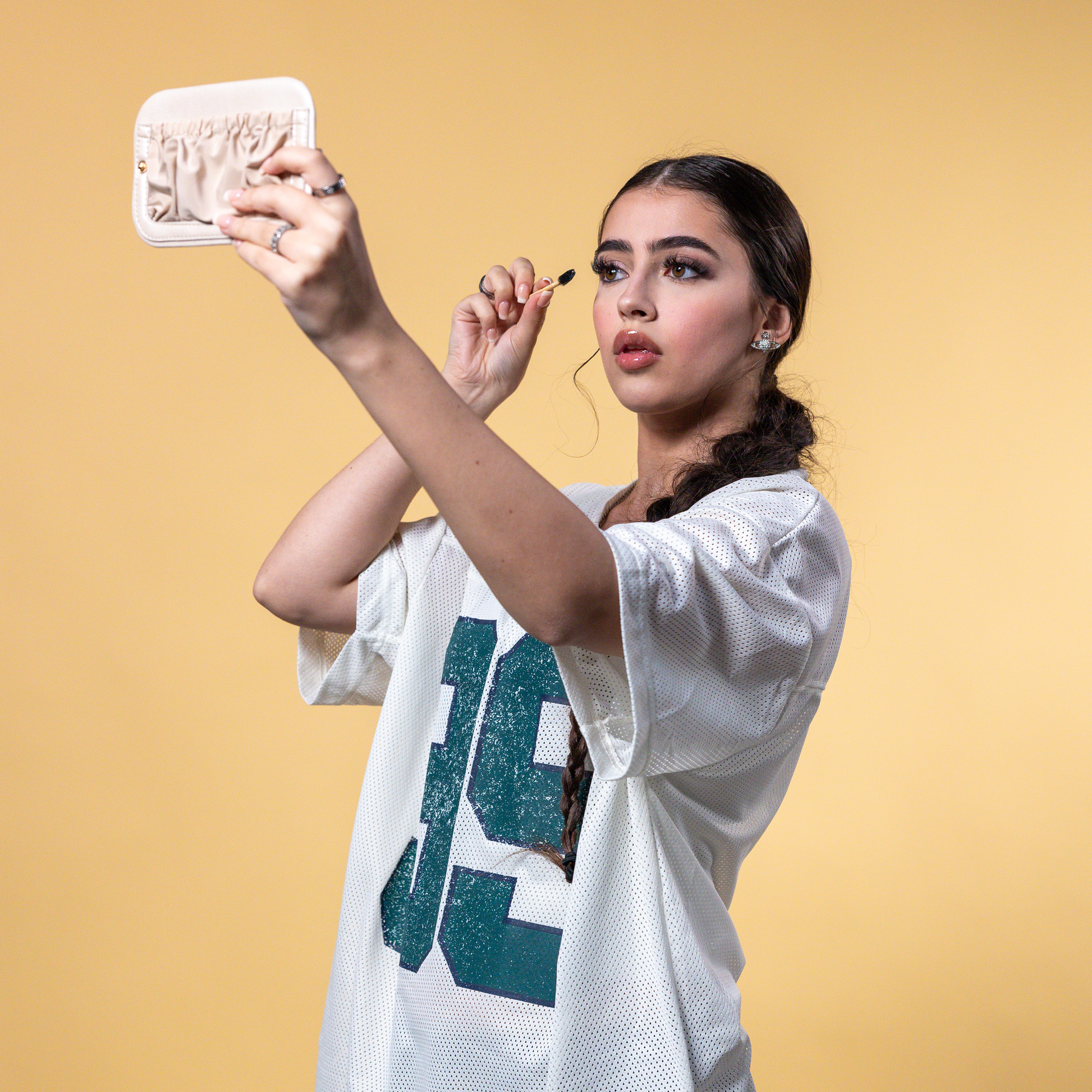Woman applying makeup in front of a mirror with a yellow background