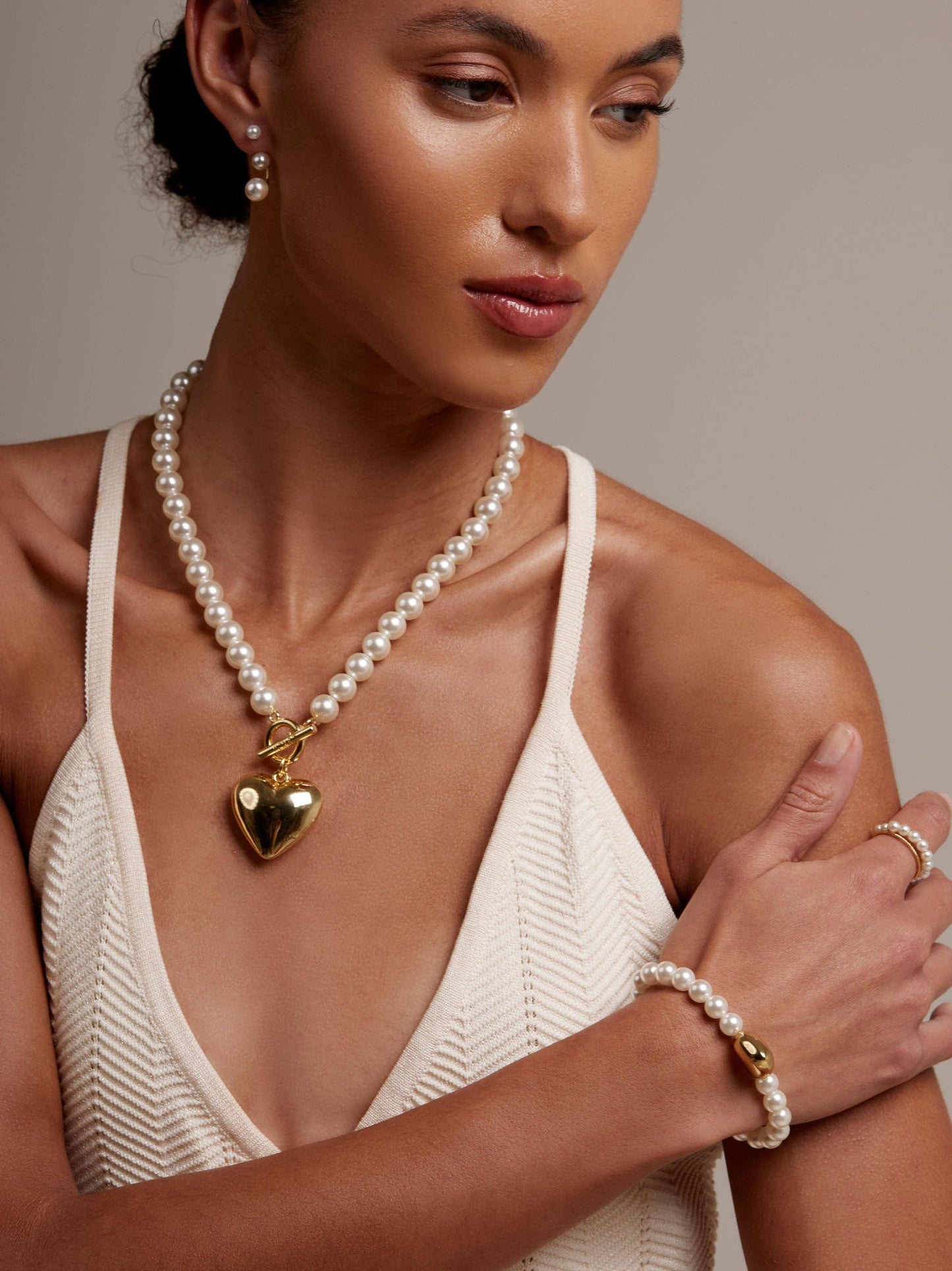Woman wearing a pearl necklace with a heart pendant and matching bracelet against a neutral background