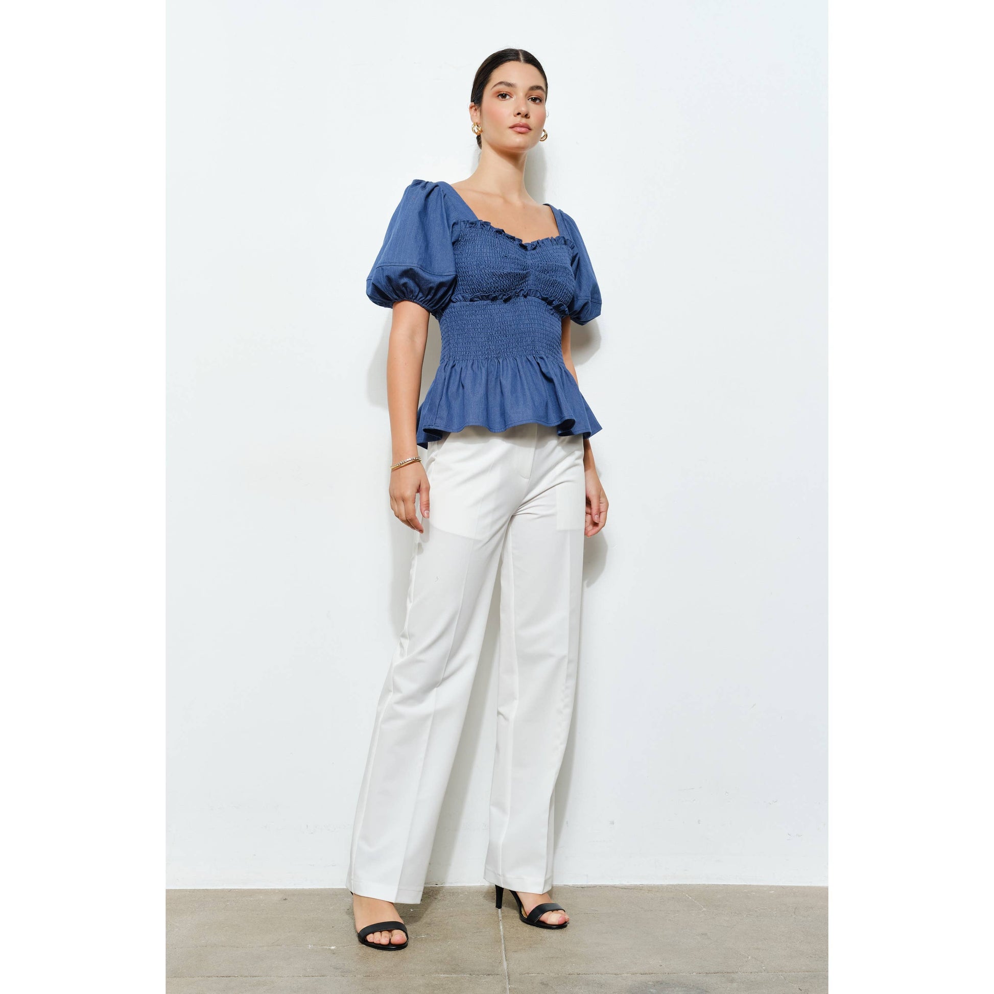 Woman wearing a blue top and white pants on a light gray background