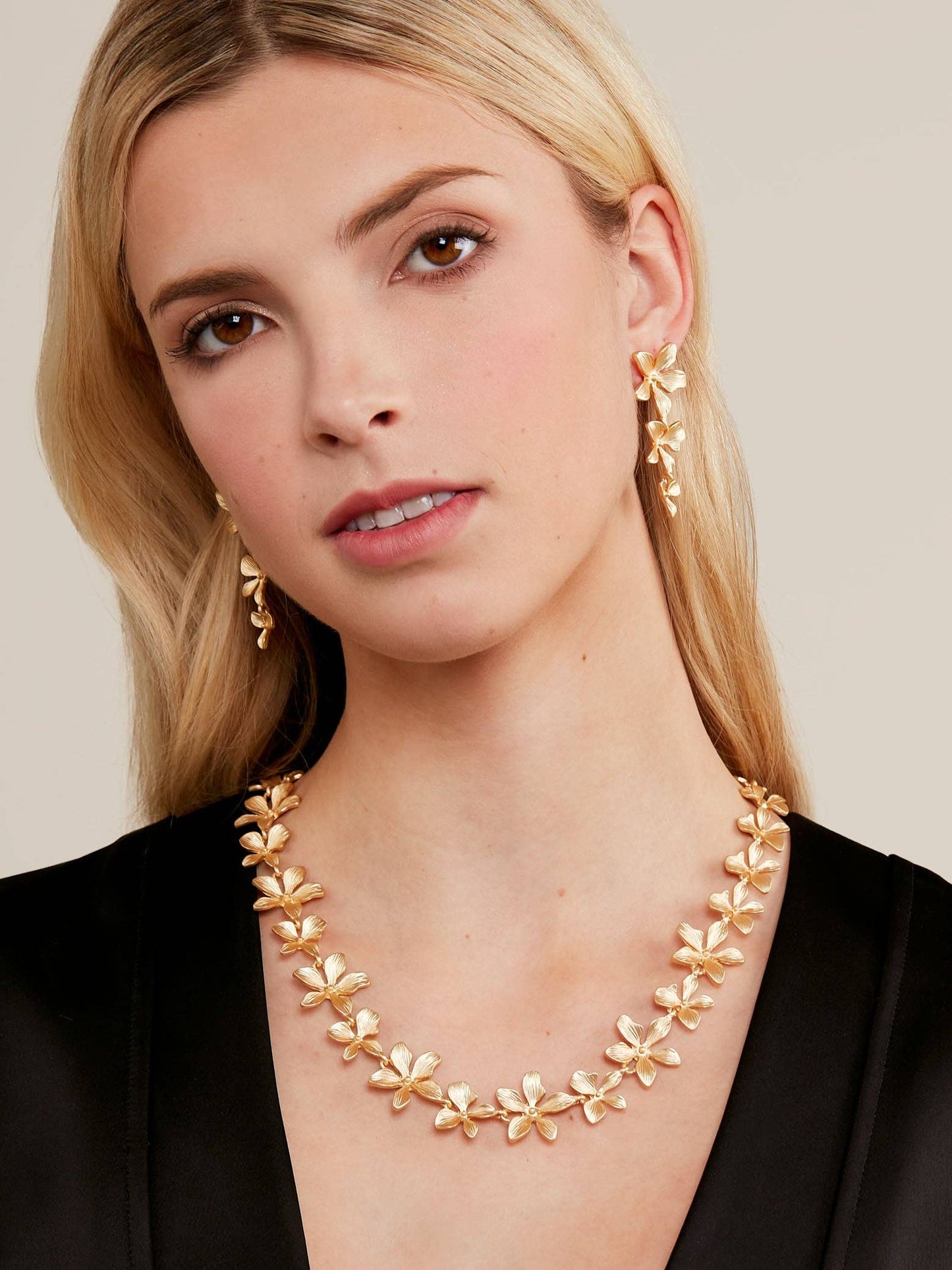 Woman wearing a gold necklace and earrings against a neutral background